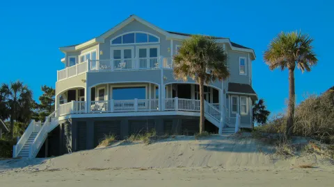 Elegant beachfront house with large windows and palm trees under clear blue sky.
