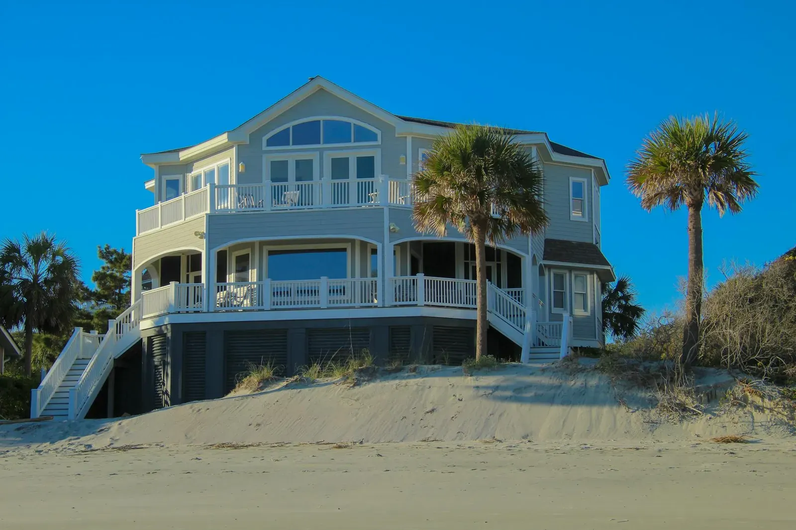 Elegant beachfront house with large windows and palm trees under clear blue sky.