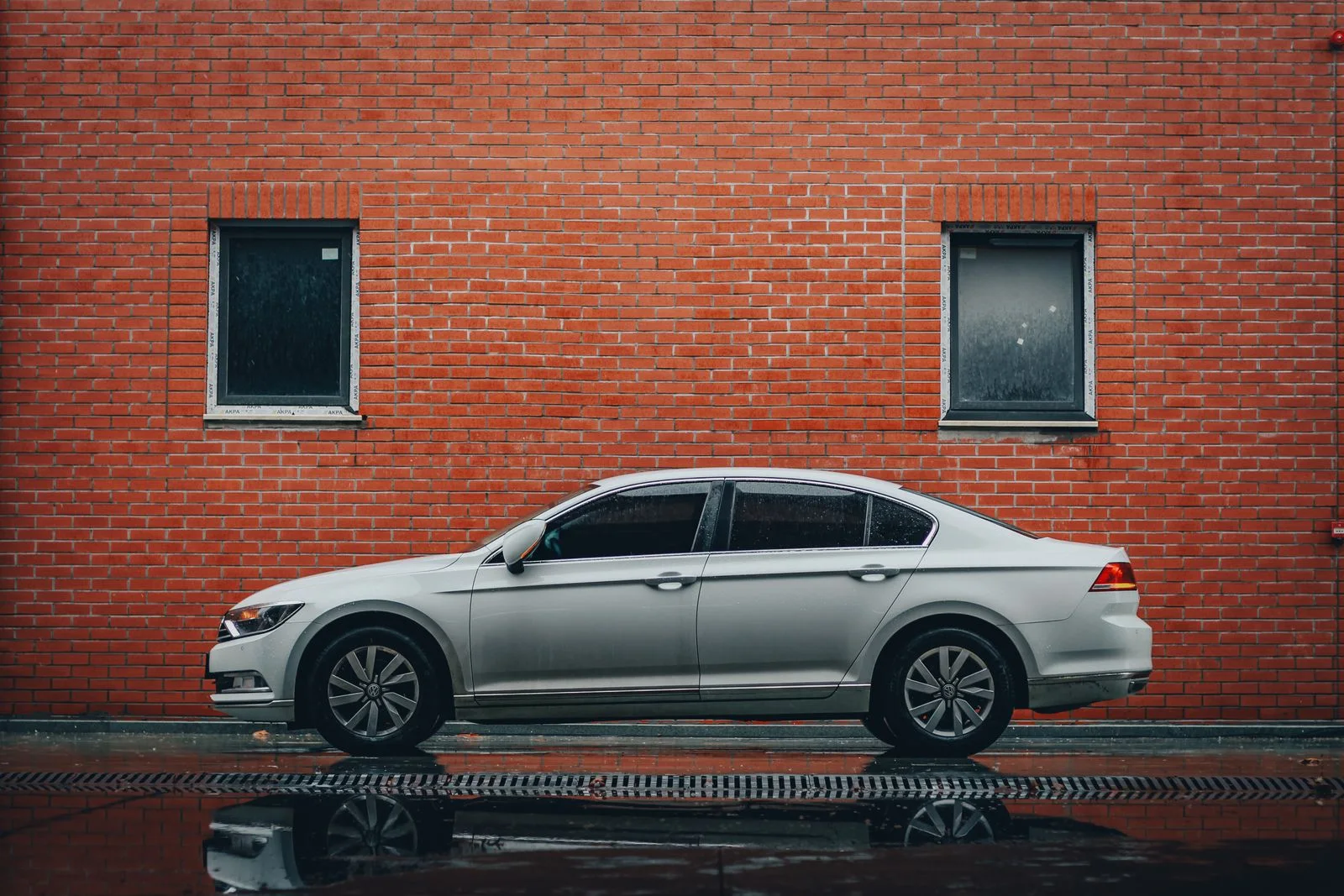 A silver sedan parked along a wet street beside a brick wall