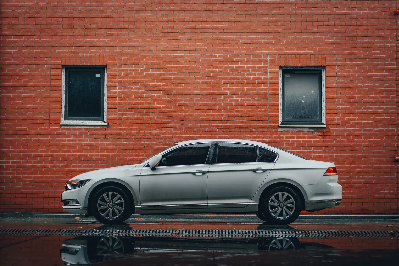 A silver sedan parked along a wet street beside a brick wall