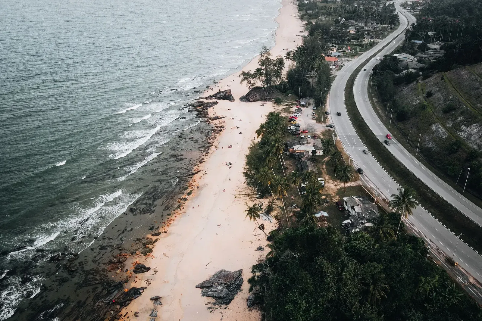 Aerial view of a picturesque coastline with winding road, palm trees, and crashing waves.