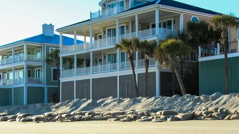 Contemporary beachfront villas with palm trees lining the sandy shore under a clear sky.