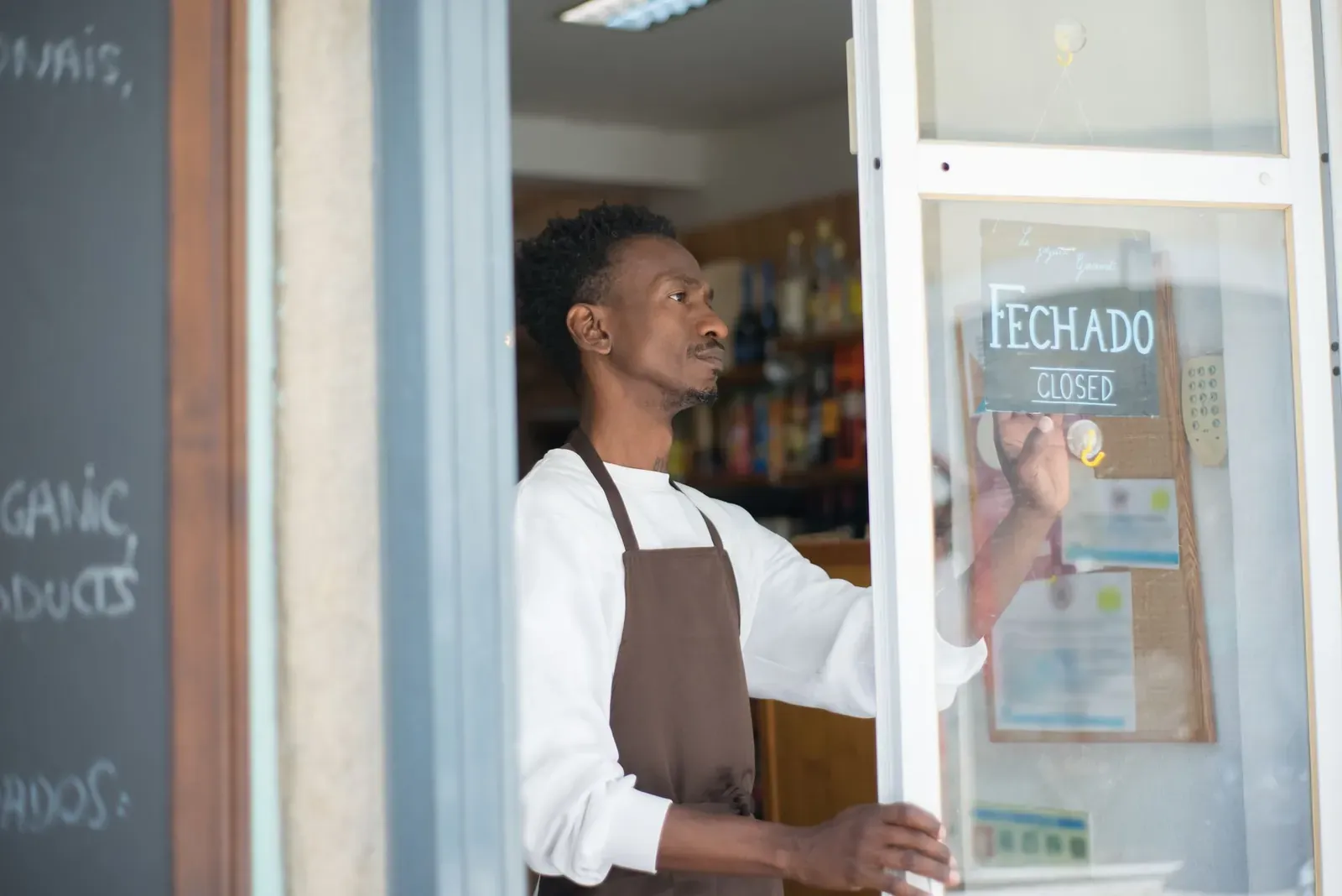 African man closing a store with a sign in Portuguese, wearing an apron.