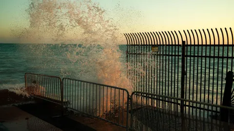 Dynamic ocean wave splashing against a metal fence at sunset in Florida.