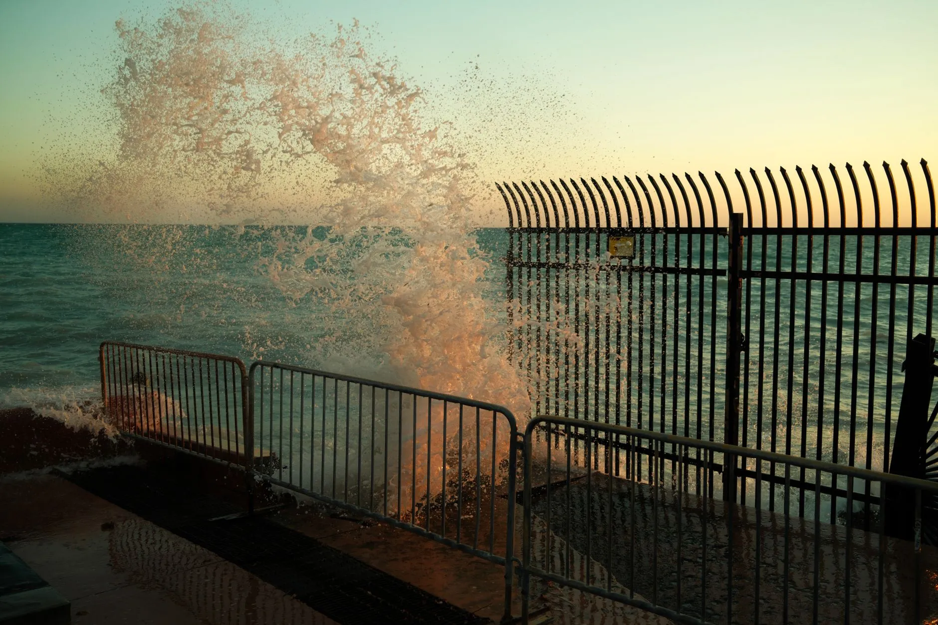 Dynamic ocean wave splashing against a metal fence at sunset in Florida.
