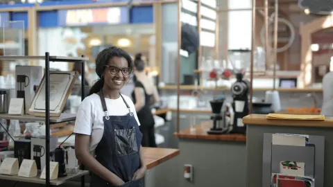 Smiling barista standing in a stylish café, showcasing entrepreneurial spirit.