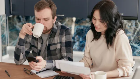 A couple reviewing bills, using a calculator and smartphone, in a modern kitchen.