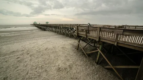 Scenic view of the wooden pier at Folly Beach, South Carolina, under a cloudy sky.