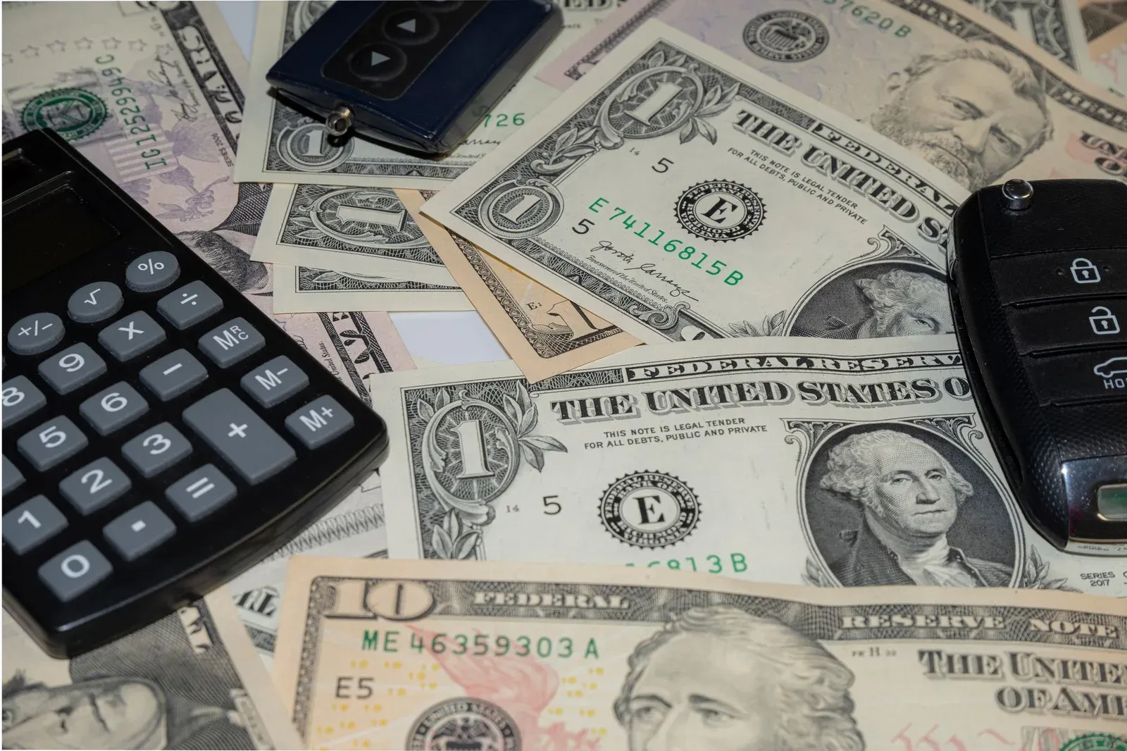 A calculator, car key, and cash on a table representing the cost of auto insurance.