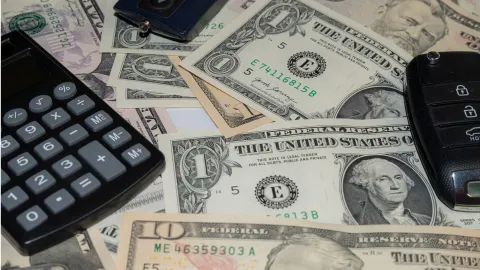 A calculator, car key, and cash on a table representing the cost of auto insurance.