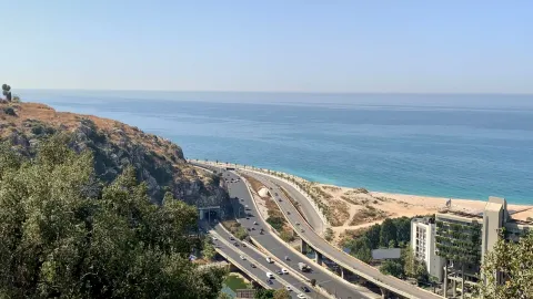 Aerial view of a coastal highway with ocean backdrop and modern buildings.