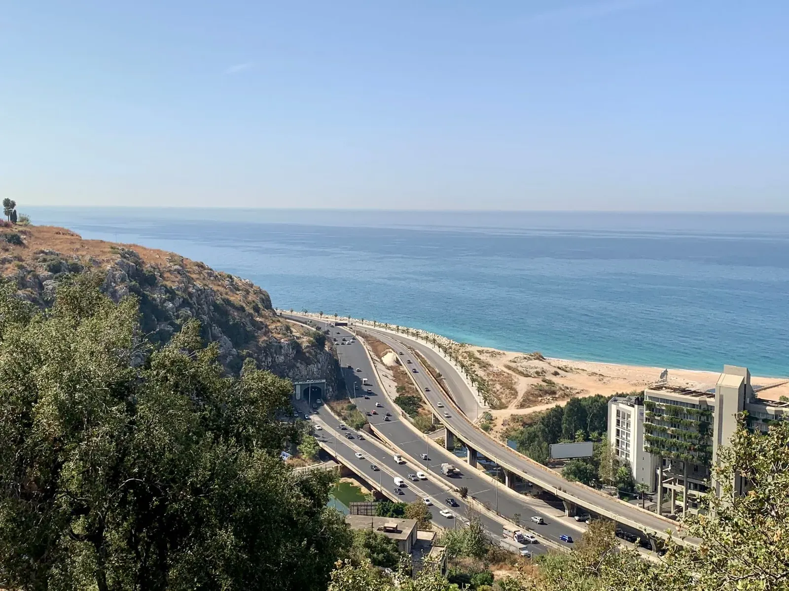 Aerial view of a coastal highway with ocean backdrop and modern buildings.