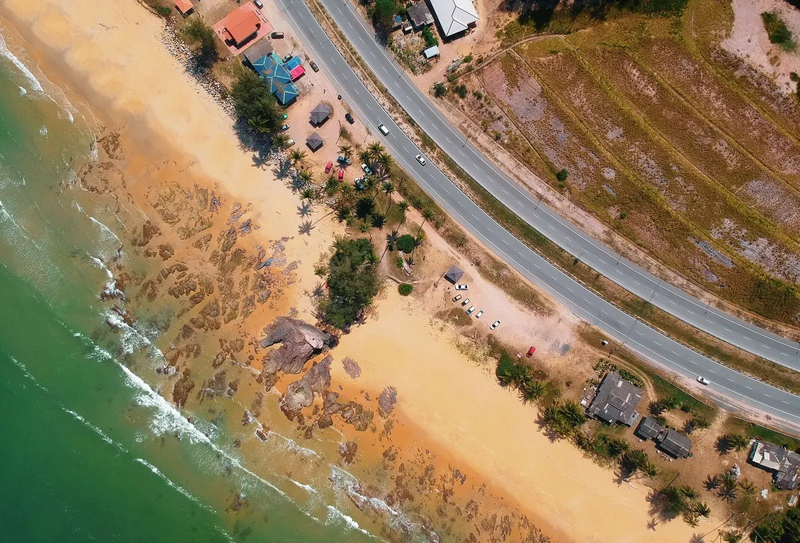 A vibrant aerial view of a scenic beach with a nearby highway and buildings during the day.