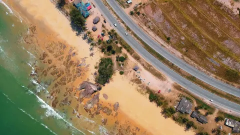 A vibrant aerial view of a scenic beach with a nearby highway and buildings during the day.