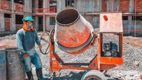 A construction worker operating a concrete mixer at an active building site, emphasizing safety gear.