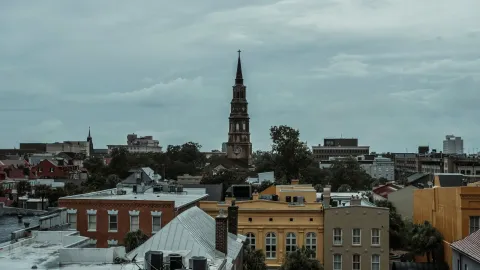 A picturesque view of Charleston, SC, featuring a historic church tower amidst vibrant buildings.