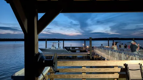 A serene evening view of the waterfront deck in Mount Pleasant, featuring people and boats under a twilight sky.
