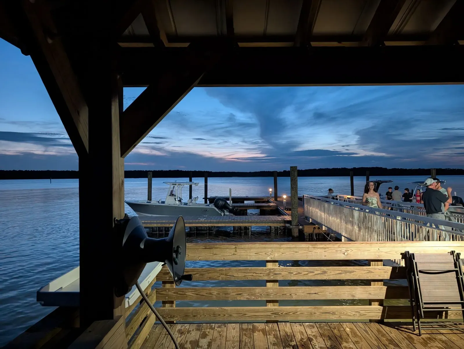 A serene evening view of the waterfront deck in Mount Pleasant, featuring people and boats under a twilight sky.