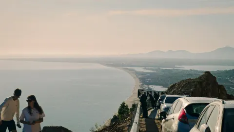 Breathtaking coastal view from Shëngjin, Albania with parked cars and people enjoying the scenery.