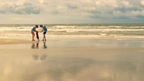 A family enjoying playtime by the shore at Sunset Beach, NC under a clear sky.