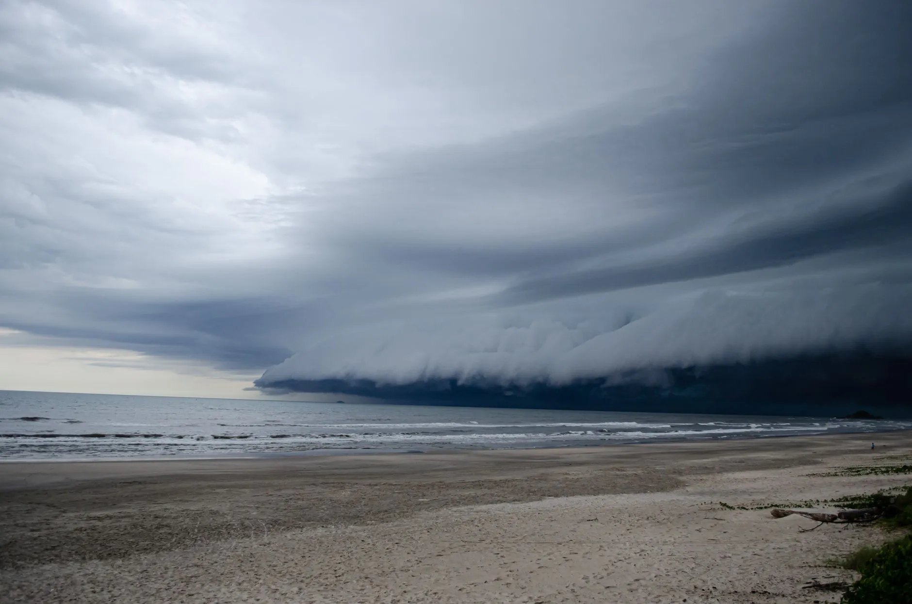 A dark storm cloud formation looms over a tranquil, deserted beach, showcasing nature's power.