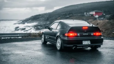 A classic car parked on a wet road beside a stormy ocean, creating a moody atmosphere.