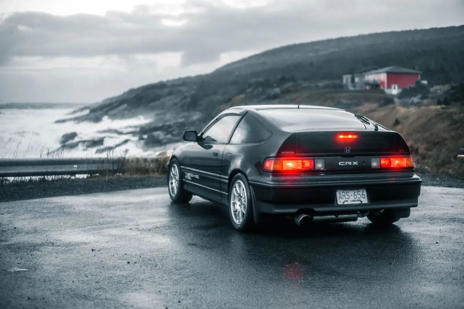A classic car parked on a wet road beside a stormy ocean, creating a moody atmosphere.