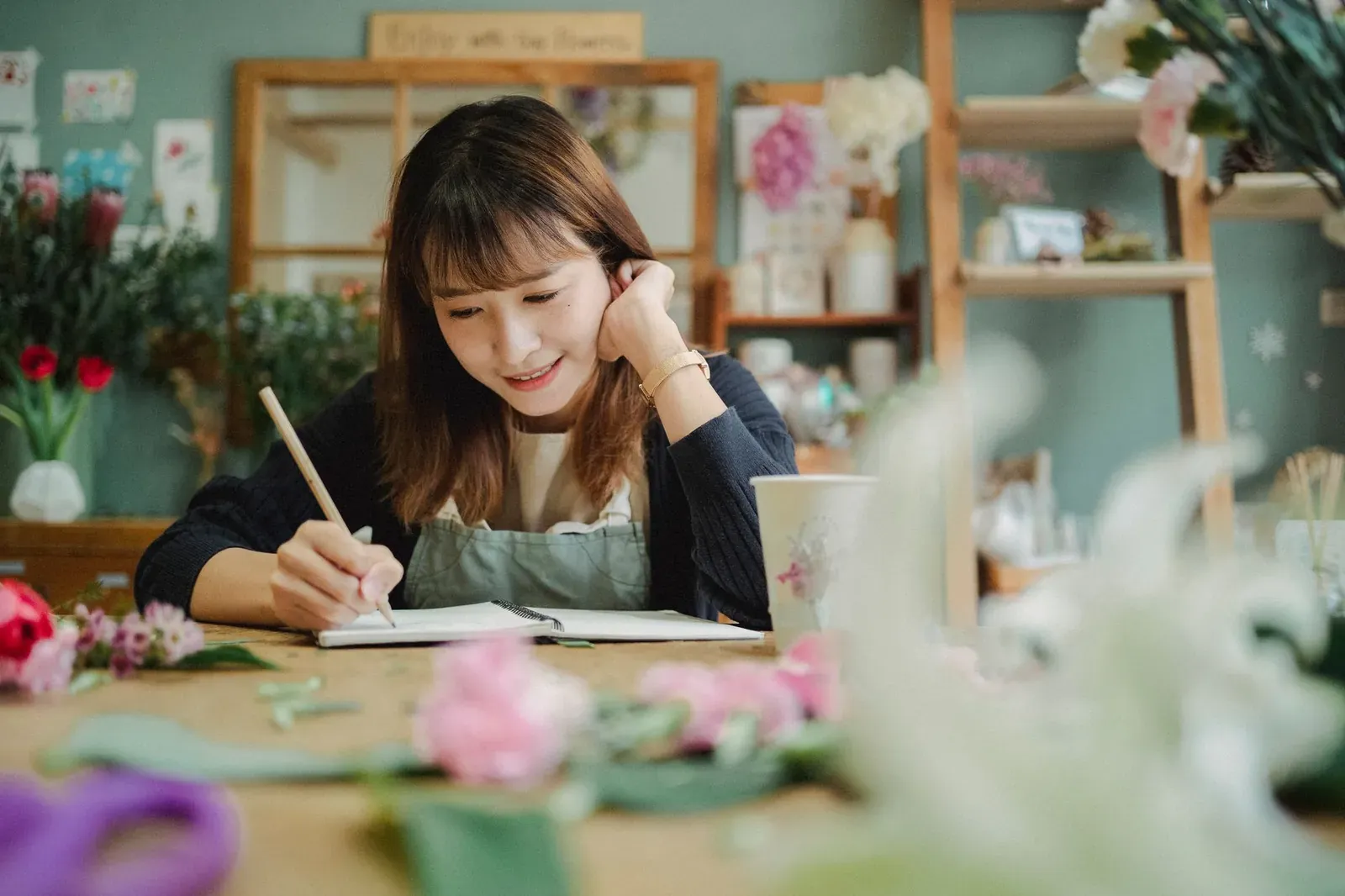 Smiling young female florist in apron writing notes while working in cozy flower shop