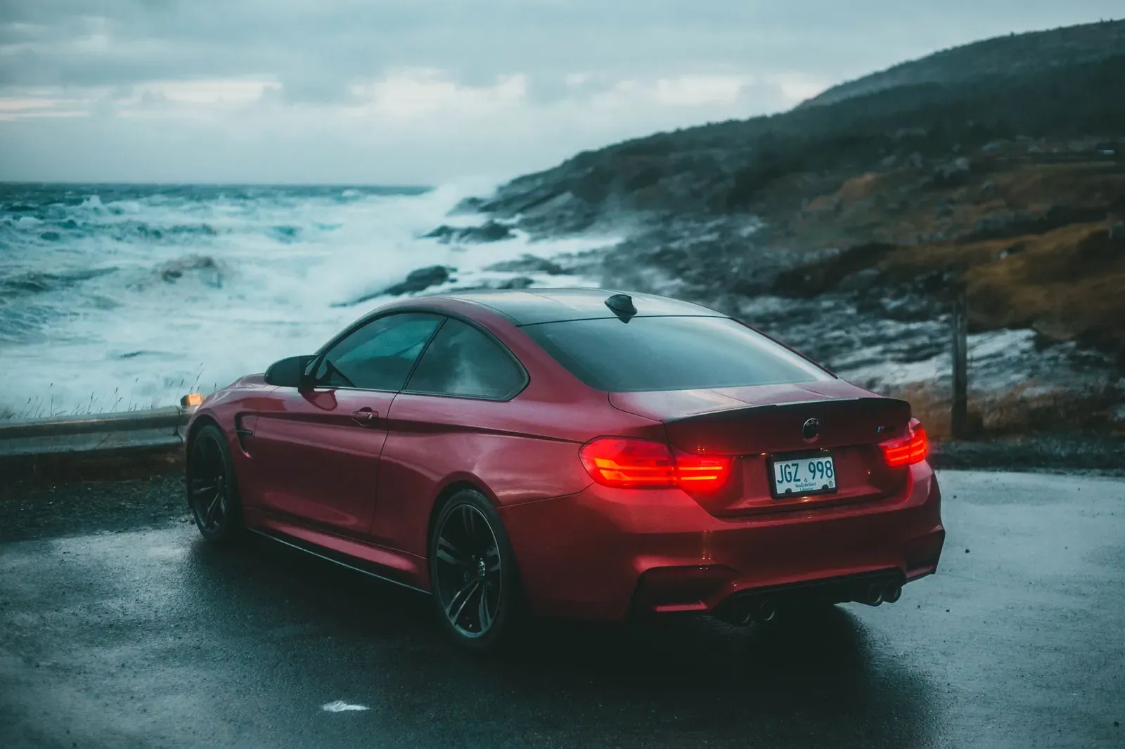 Red sports car parked by an ocean cliff during twilight, showcasing adventure travel.