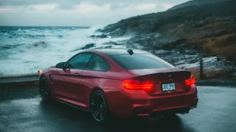 Red sports car parked by an ocean cliff during twilight, showcasing adventure travel.